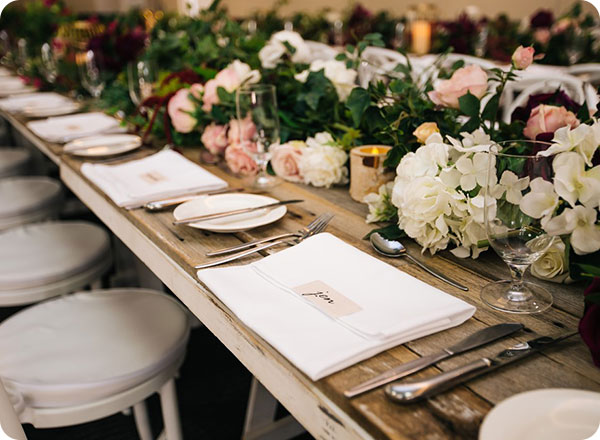 Photo shows a wooden rustic table beautifully setup with flowers and candles for a wedding